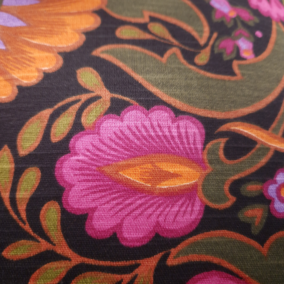 Détail du tissu vintage en coton du coussin Boho Folk, motif floral des années 70 fuchsia, orange et vert olive sur fond noir.