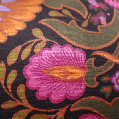 Détail du tissu vintage en coton du coussin Boho Folk, motif floral des années 70 fuchsia, orange et vert olive sur fond noir.