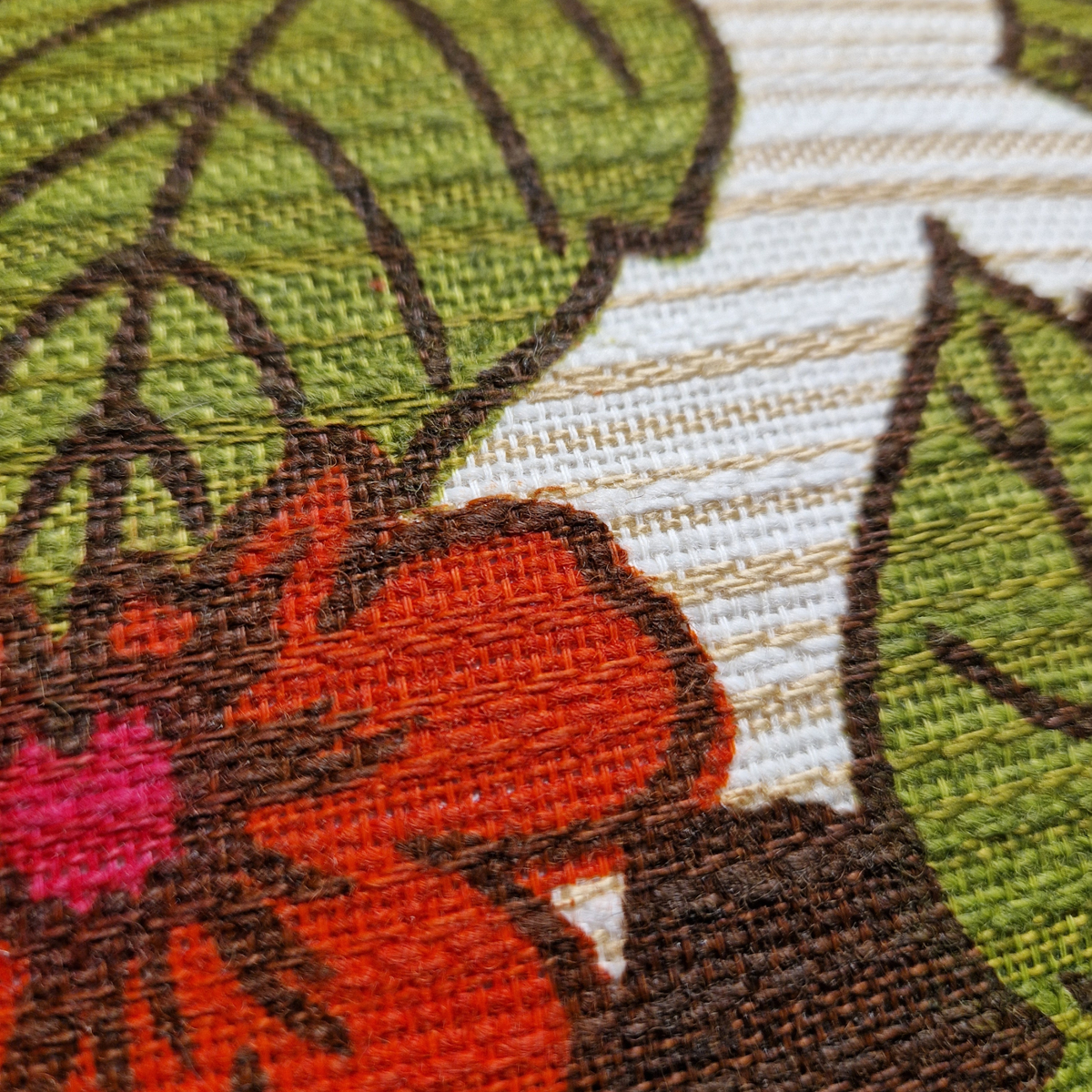 Détail de la texture du tissu vintage années 70 du coussin Dahlia avec motif floral rouge et feuillage vert