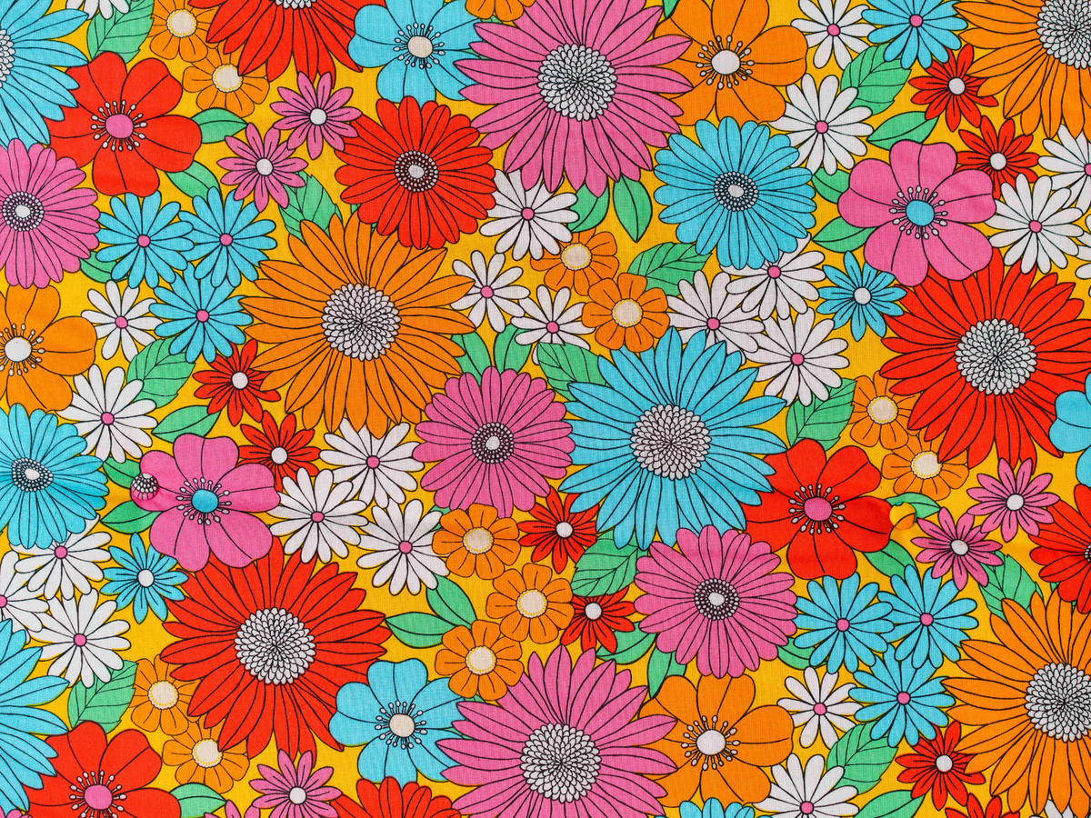 Vue rapprochée du motif floral multicolore du matelas de plage Bloom ’72, fleurs orange, roses, bleues et blanches sur fond jaune avec boutons recouverts