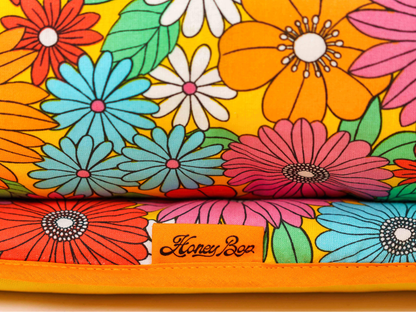 Détail du tissu floral multicolore du matelas de plage Bloom ’72, avec fleurs orange, roses, bleues et blanches et étiquette Honey Bop