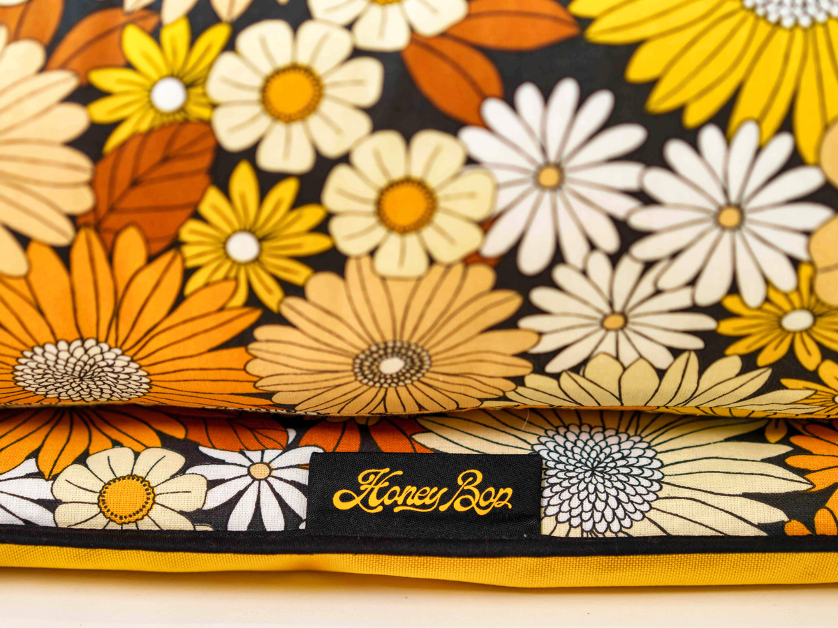 Détail du motif floral du matelas de plage Golden Bloom ’72, dans les tons jaune, orange, crème et marron, avec étiquette Honey Bop