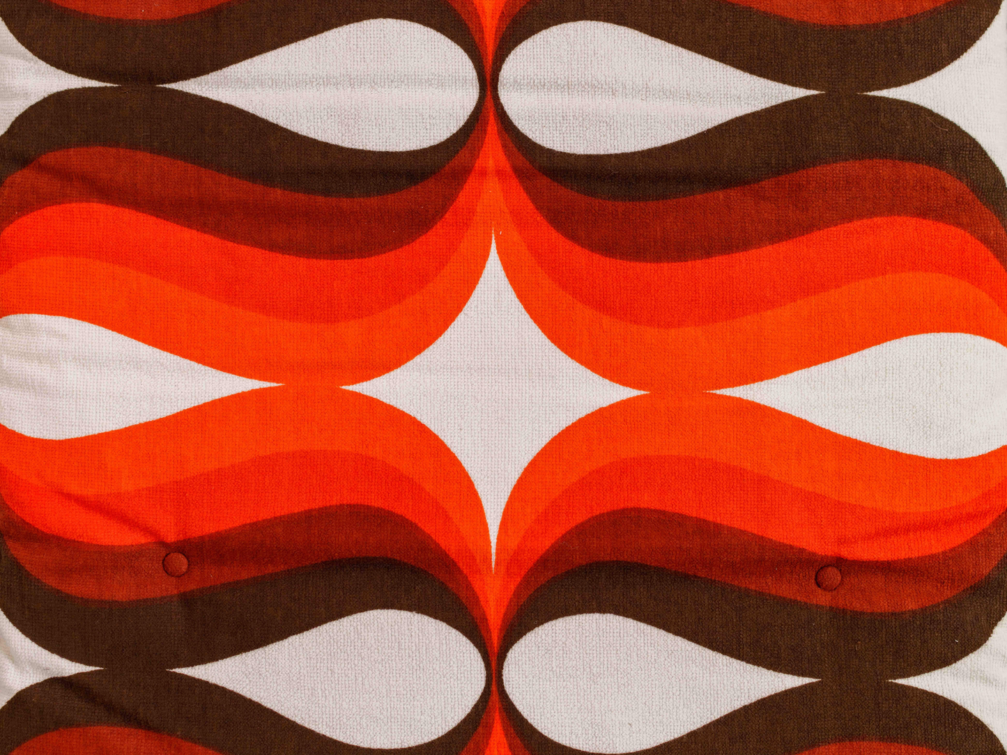 Gros plan du tissu éponge vintage du matelas de plage Riviera ’74, motif géométrique orange, marron et blanc des années 70 avec boutons recouverts